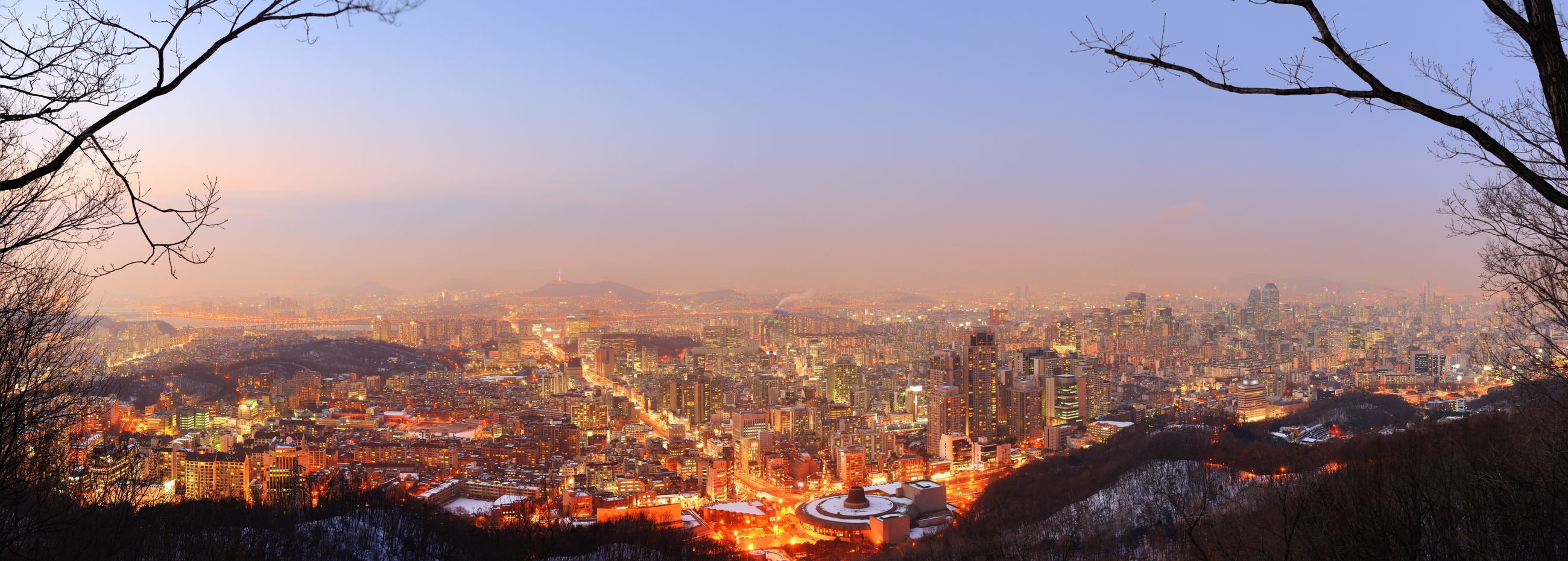 Panoramic dusk view of the Seoul skyline from Namsan, city lights coming on beneath a fading sunset
